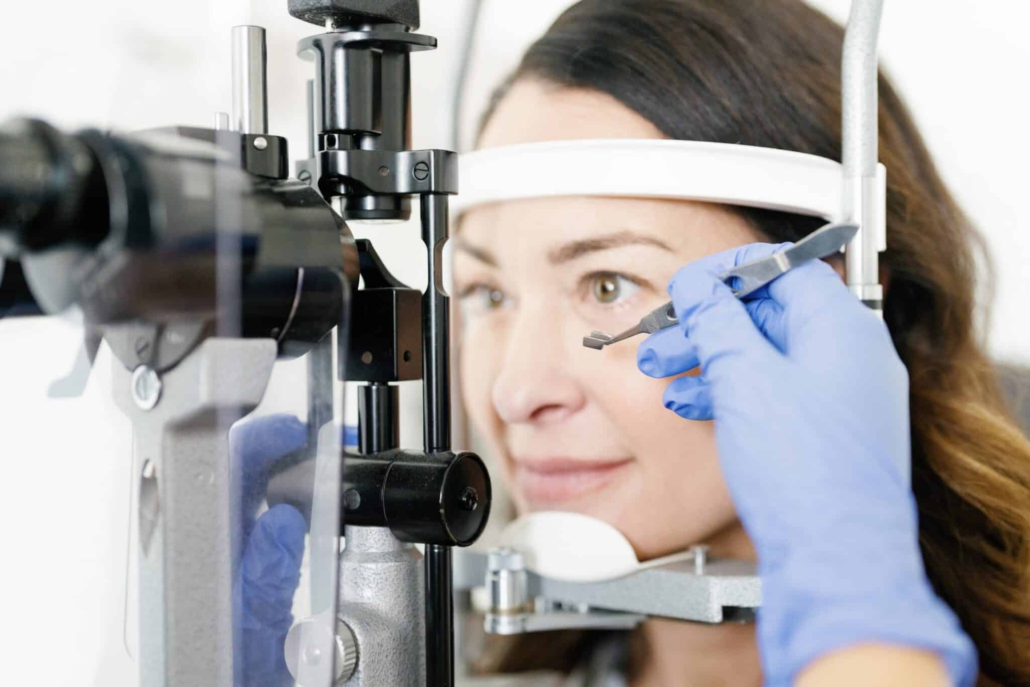 female patient undergoing eye exam with ophthalmologist's hand holding small instrument near eye