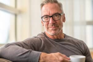 A middle-aged man wearing glasses holding a cup of coffee.