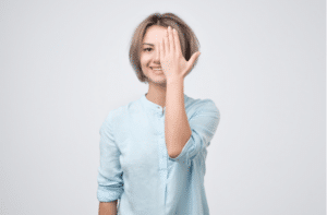 young woman in blue shirt closing one eye with hand and smiling.