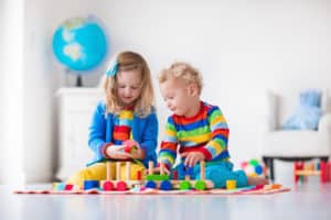 Toddler kid and baby play with blocks trains and cars.