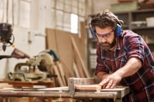 Skilled carpenter using a circular saw and wearing safety googles and earmuffs