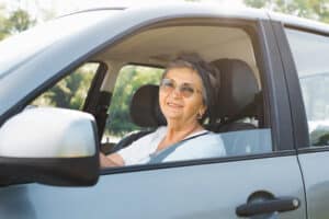 Elderly woman with glasses behind the wheel of a car, unsure if she should be driving with cataracts.
