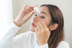 A woman putting eyedrops in her eyes to address dry eyes