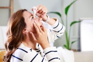 Side view of a woman putting in eye drops to combat her chronic dry eye symptoms
