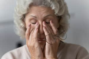 Older woman with blurry vision rubbing her eyes, possibly suffering from cataracts
